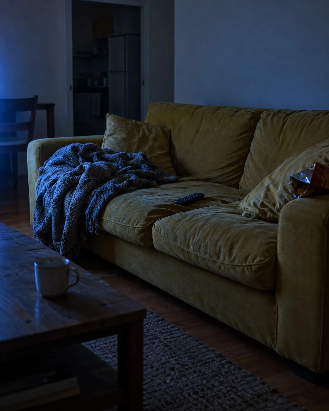 Um sofá mostarda vazio com um comando de televisão numa sala à meia-luz
